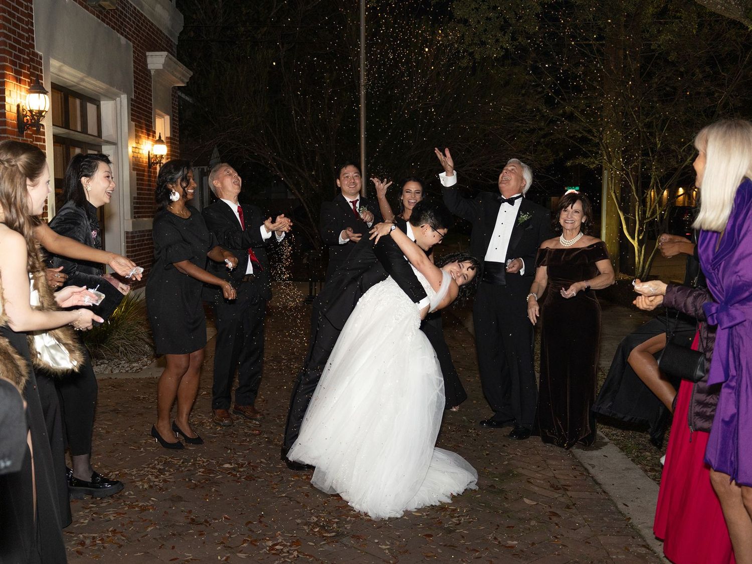 Wedding guests dance and celebrate on a dimly lit outdoor patio during an evening reception.