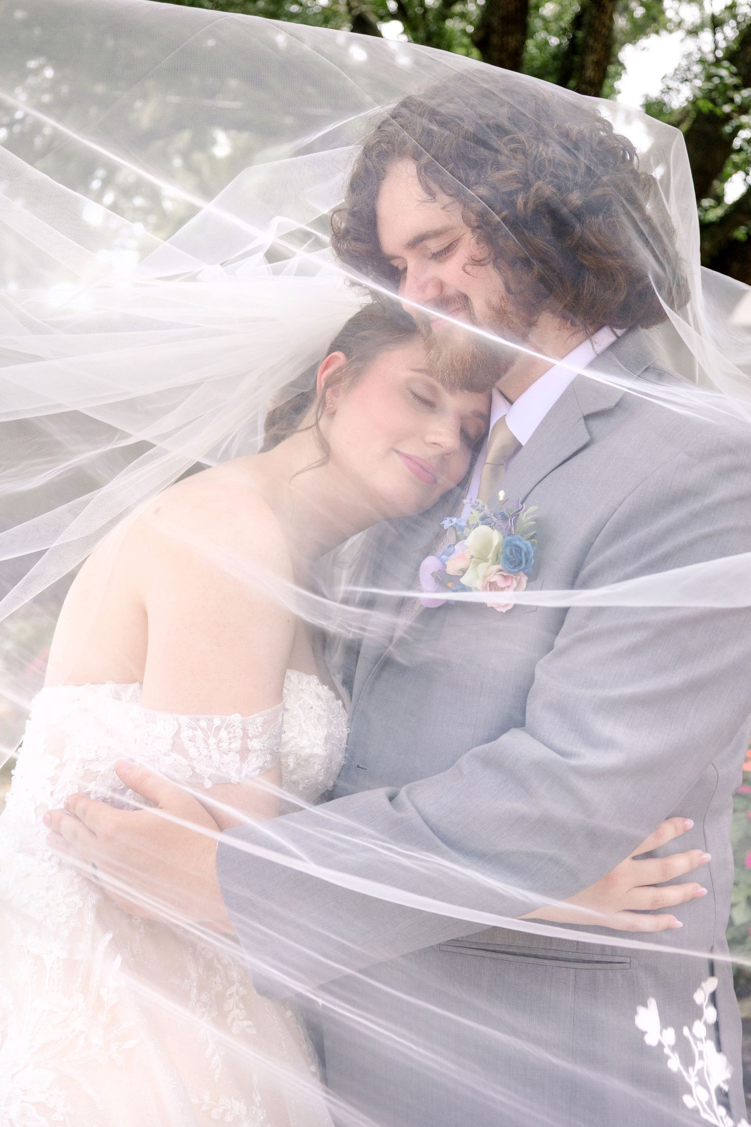 Romantic moment under flowing veil with couple in wedding attire.