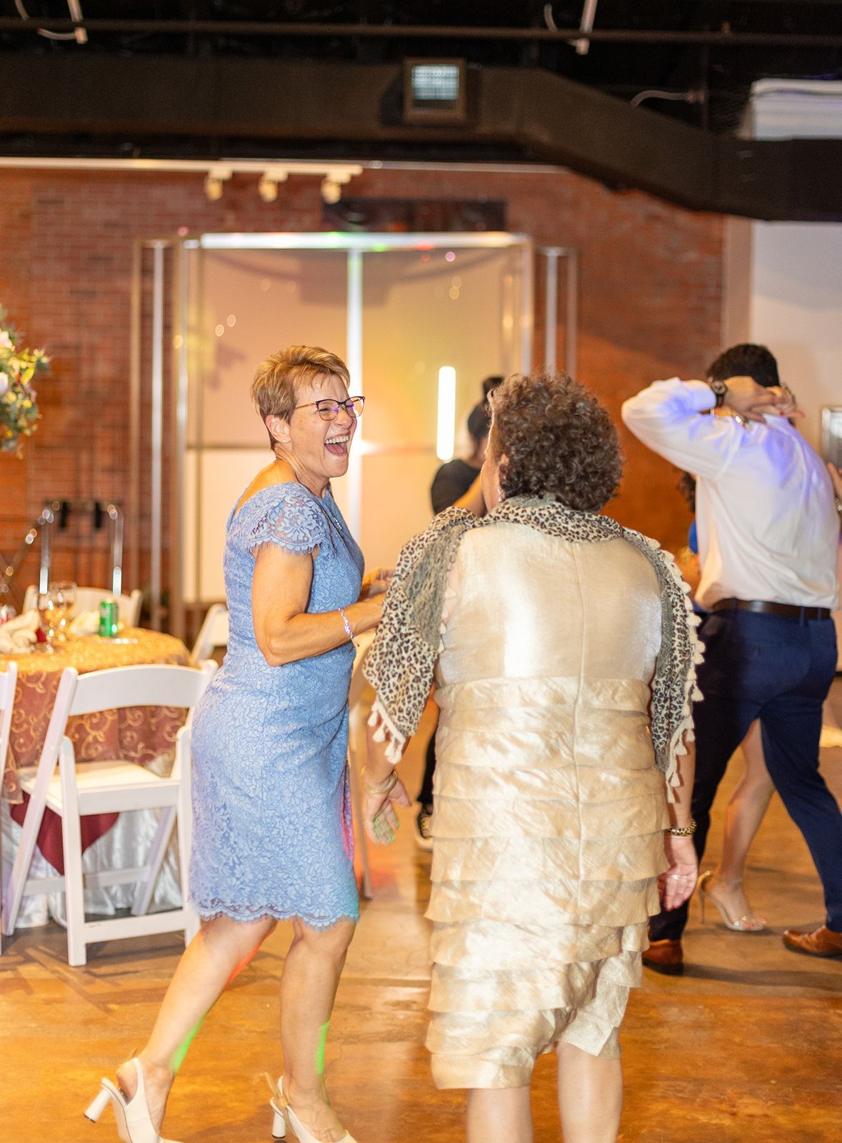 Guests dancing joyfully at a wedding reception in a rustic brick-walled venue.