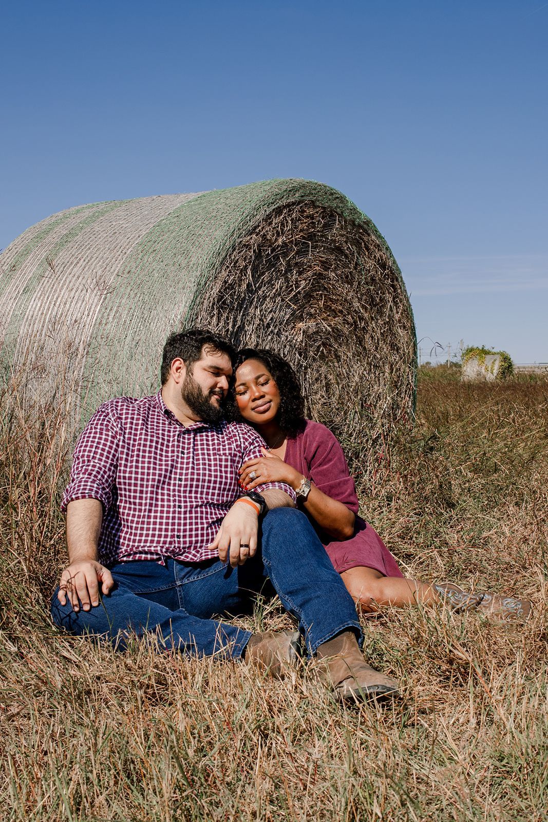 Couple cuddling and enjoying intimate moments while resting against hay bales in a rural field.