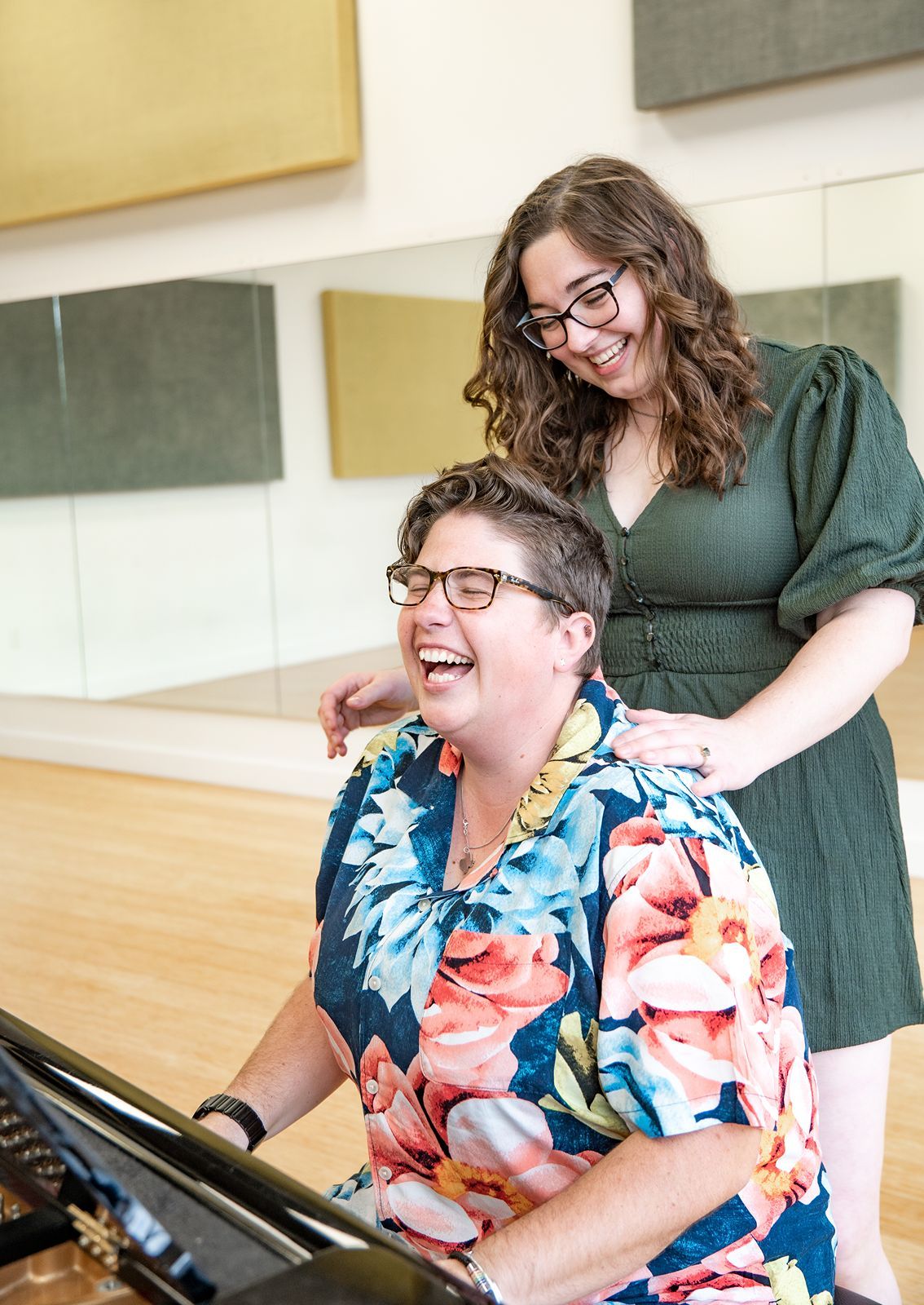 Two musicians share a joyful moment while seated at a piano in a bright studio space.
