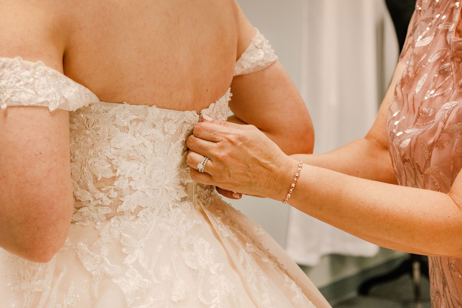 Final adjustments being made to a white lace wedding dress in a bridal fitting room.