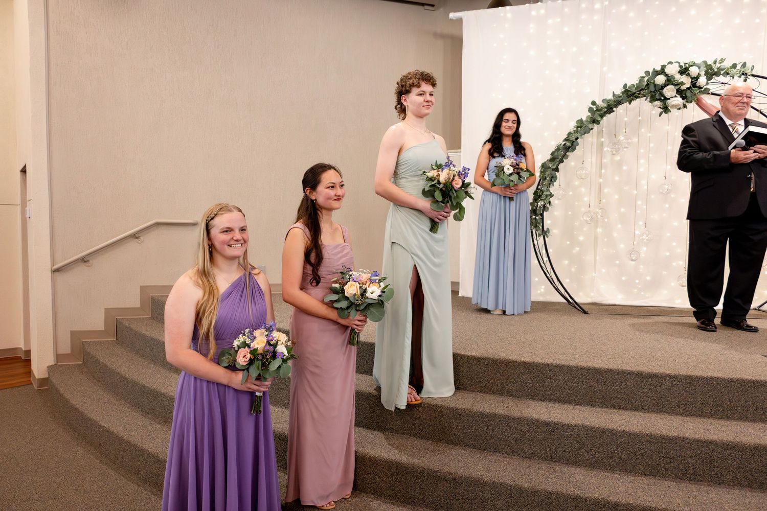 Wedding party members stand on tiered steps in a modern church sanctuary.