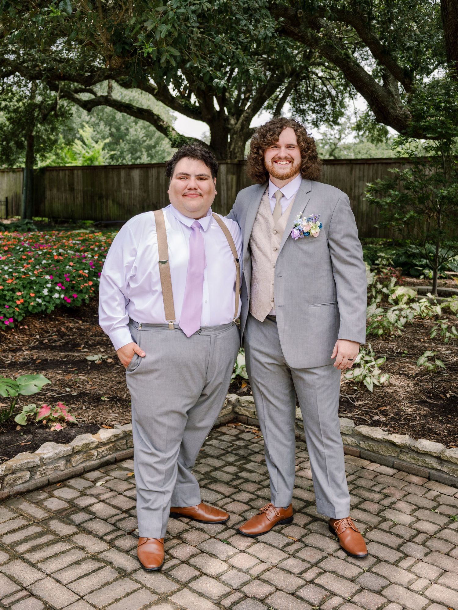 Wedding attendants in matching gray suits and pink accessories posing in a garden setting.