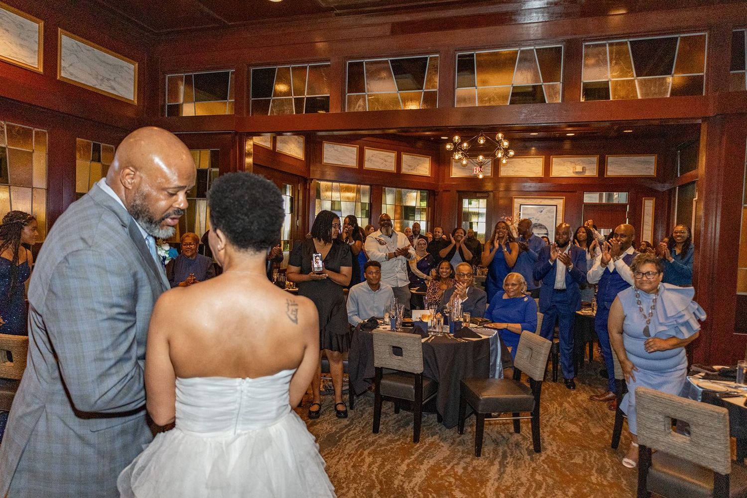 Bride and groom face cheering guests dressed in blue at elegant indoor wedding reception.