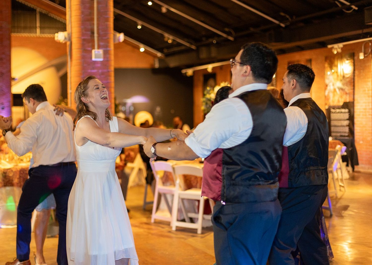 Wedding guests joyfully dancing together on the dance floor at indoor reception.