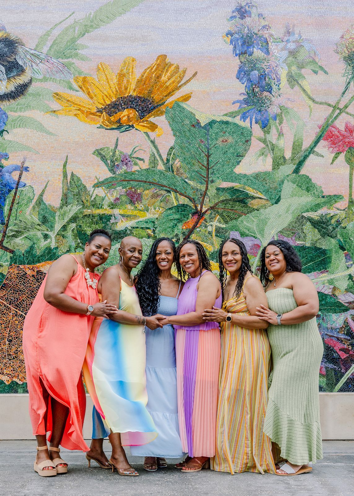 A group in colorful pastel dresses poses together against a floral mural backdrop in three similar shots.