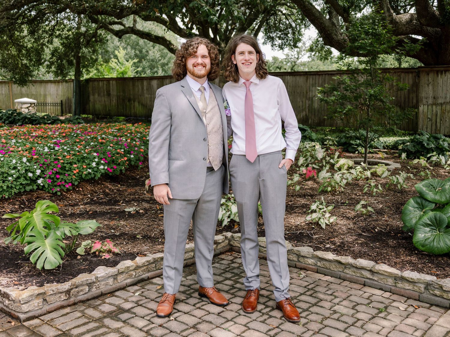 Group photo of wedding party in gray suits posing on garden brick pavers.