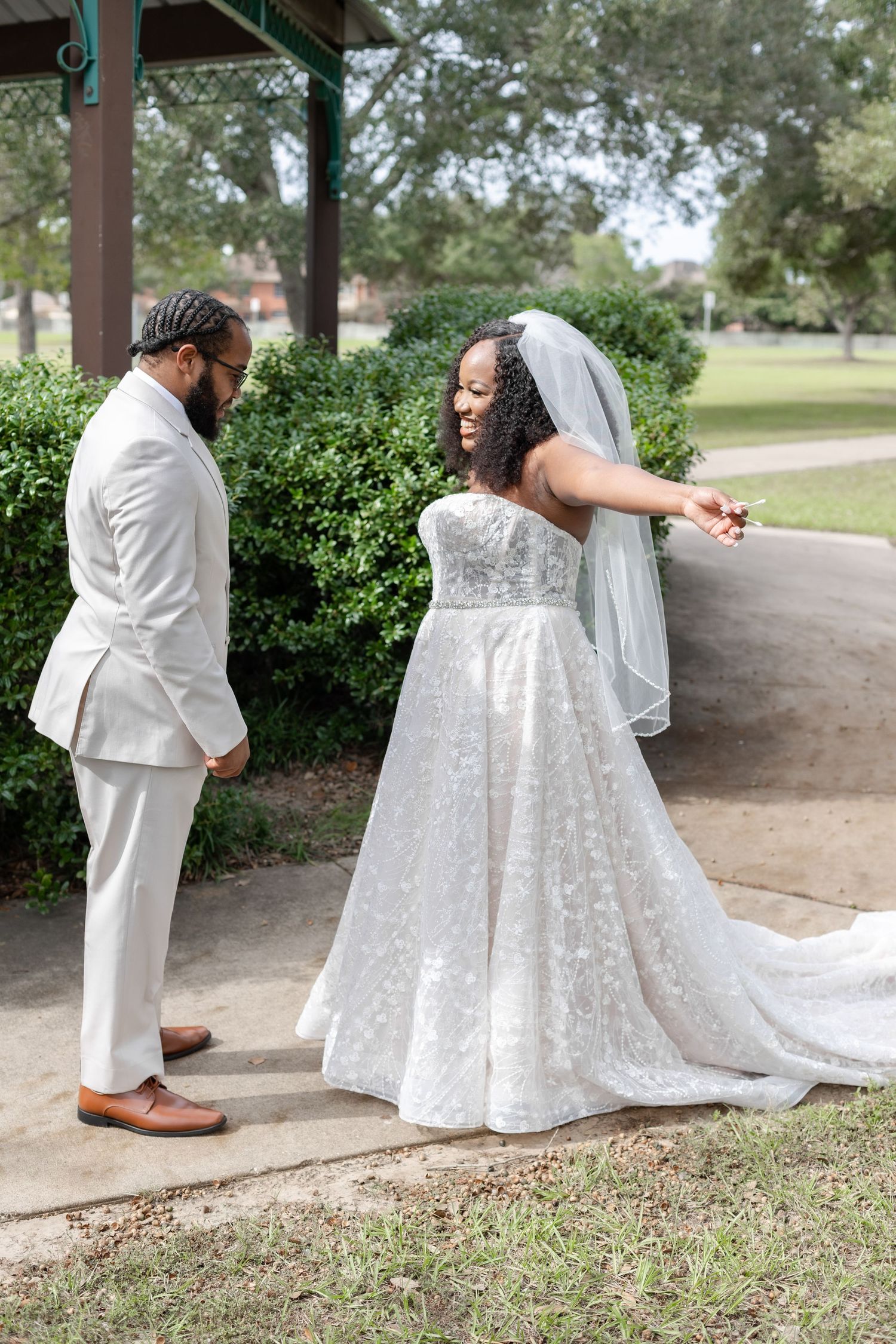 Beautiful wedding couple wearing white poses playfully in an outdoor garden setting.