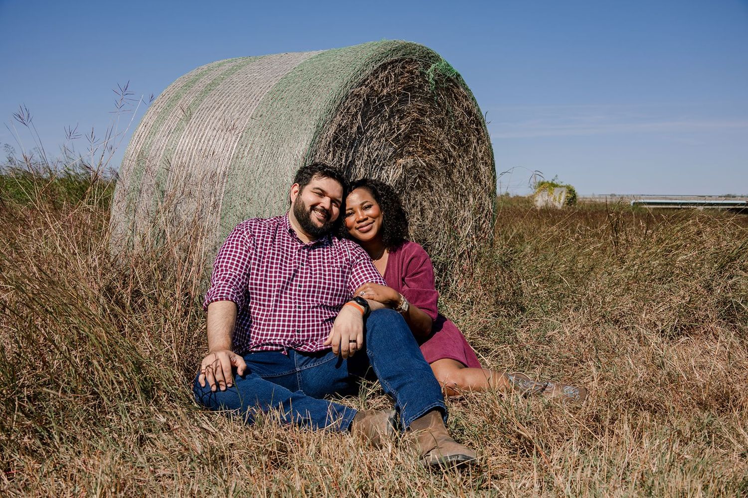 Happy couple laughing and embracing on a sunny day in front of large hay bales.