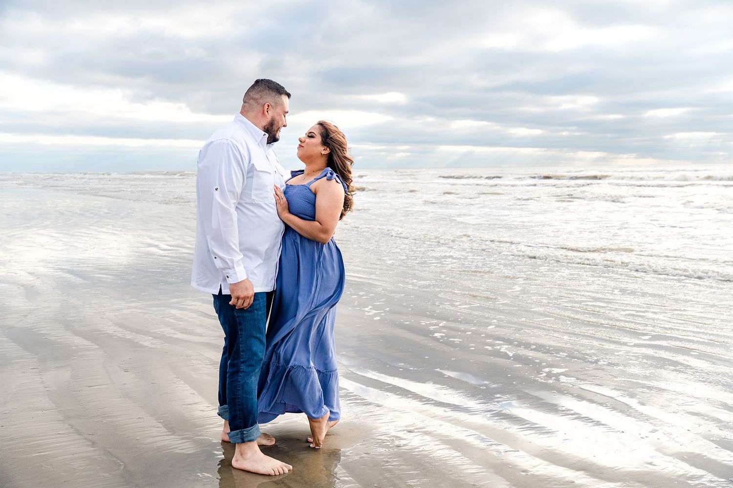 Romantic couple embraces during sunset photoshoot at beach with waves rolling in background.