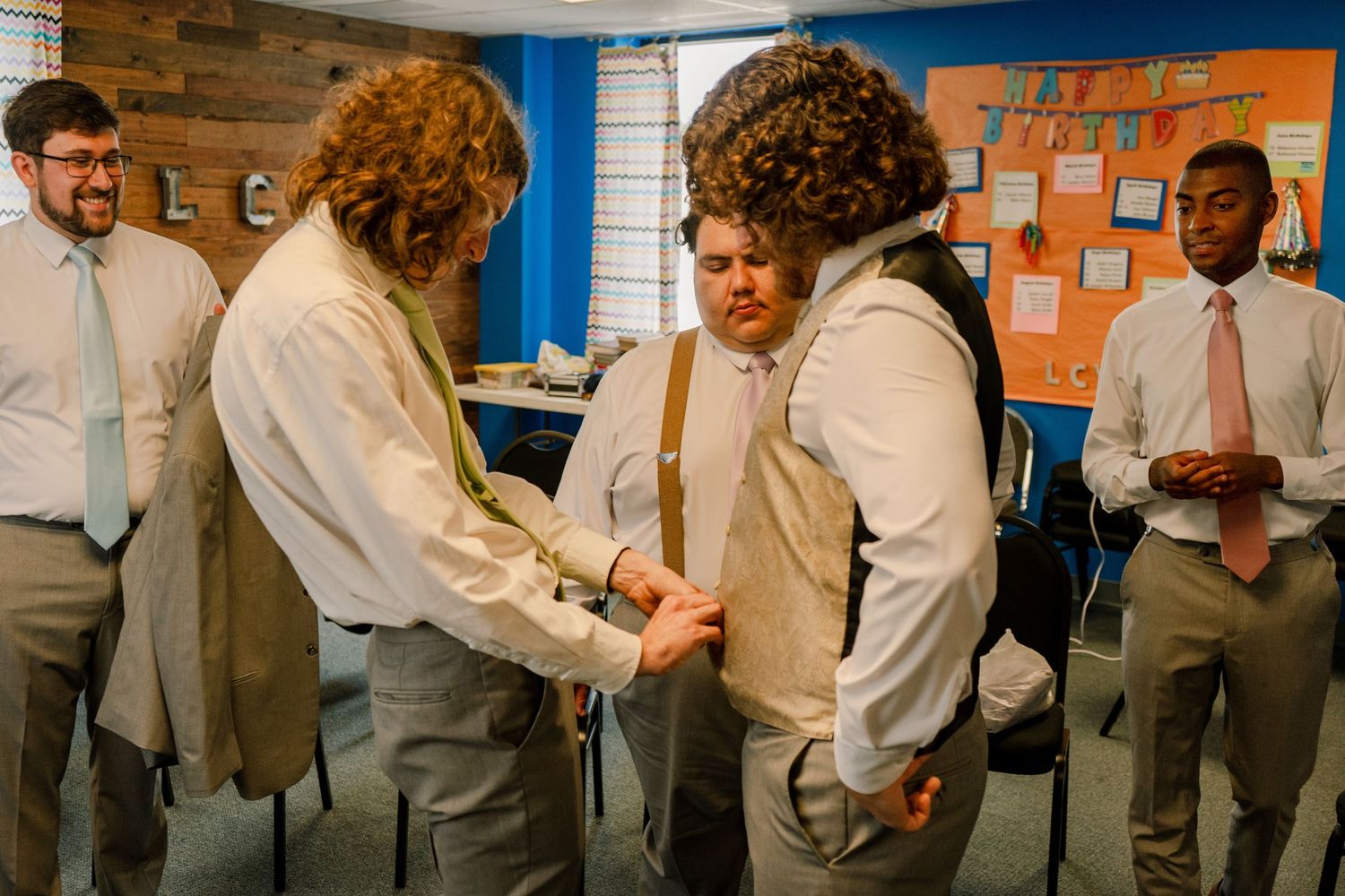 Groomsmen in white shirts and gray pants sharing candid moments in a room with blue walls.
