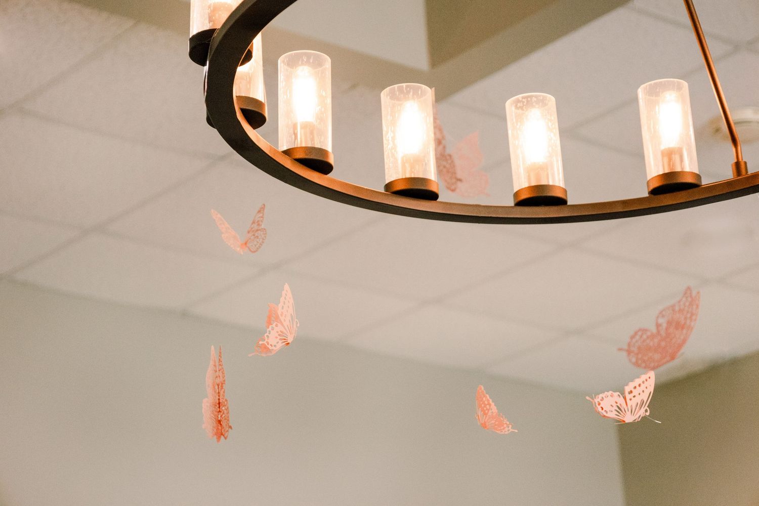 Elegant chandelier lighting with hanging pink paper butterflies in an event space.