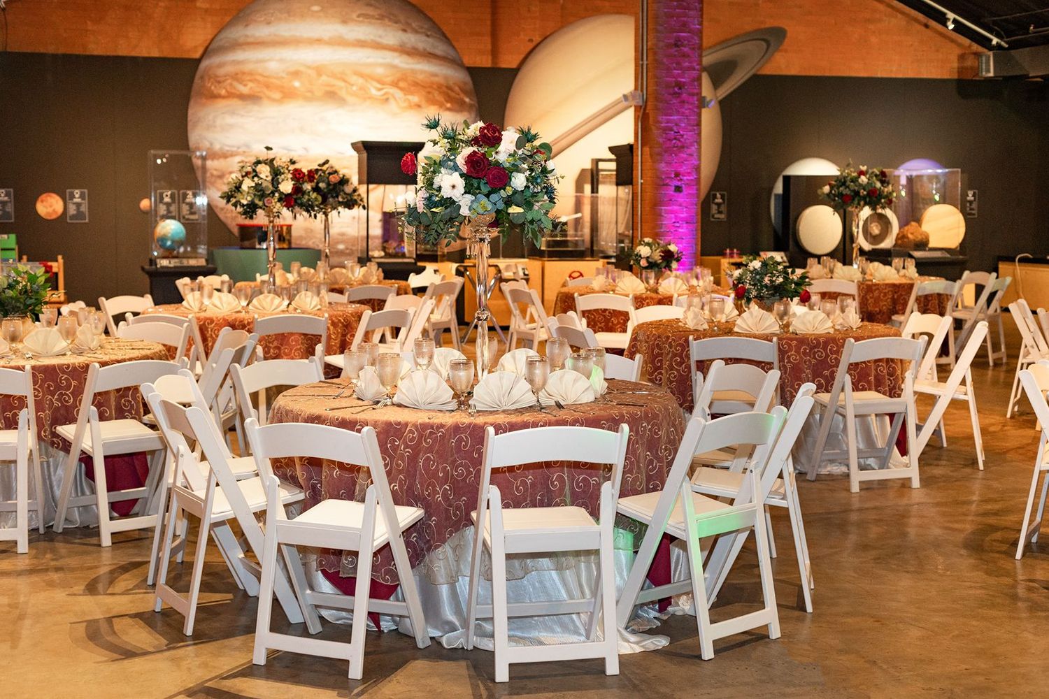 Elegant wedding reception with round tables, white chairs, and planet decor in a museum venue.