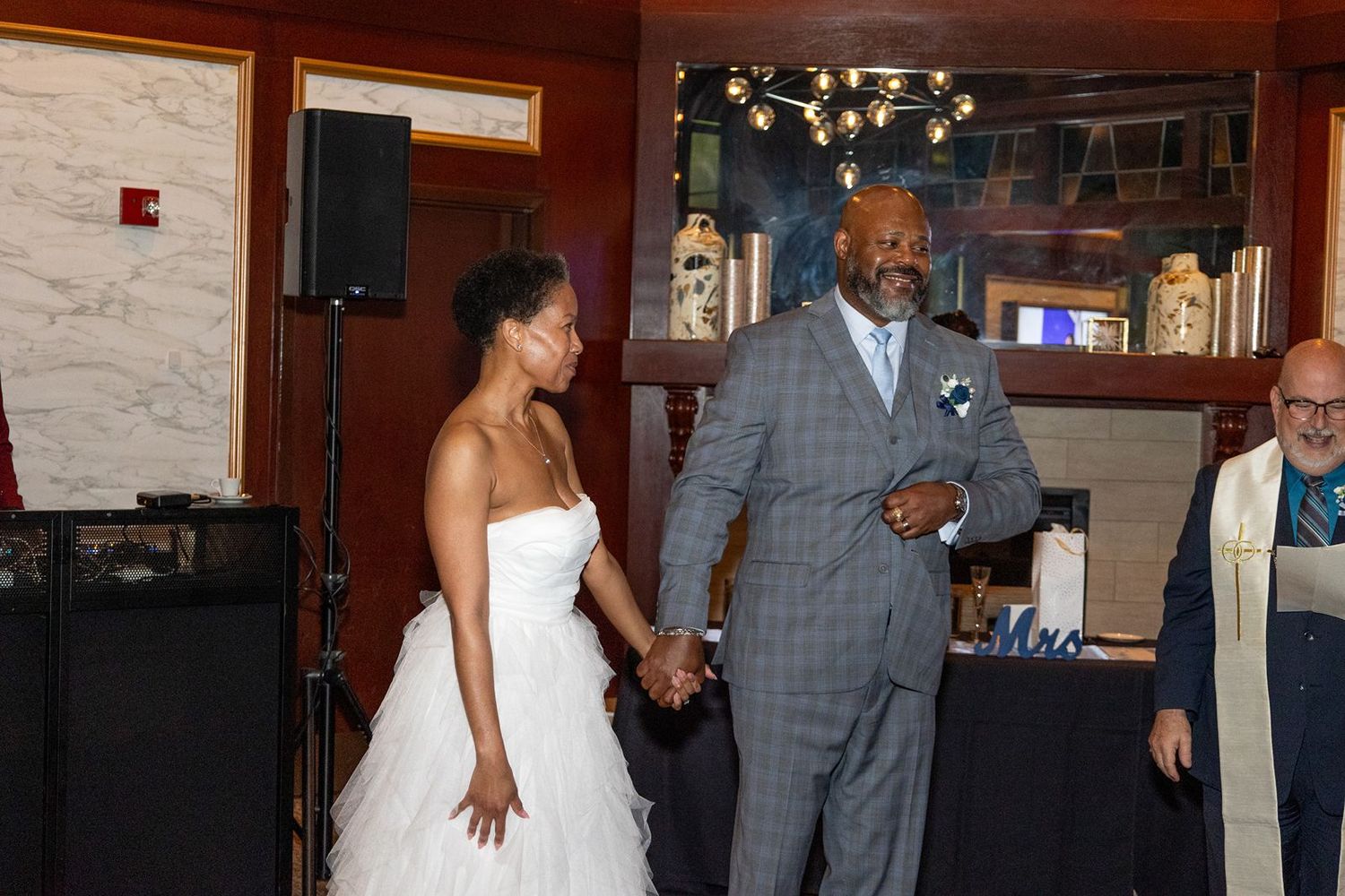 Bride in white gown and groom in gray suit hold hands during wedding reception dance.
