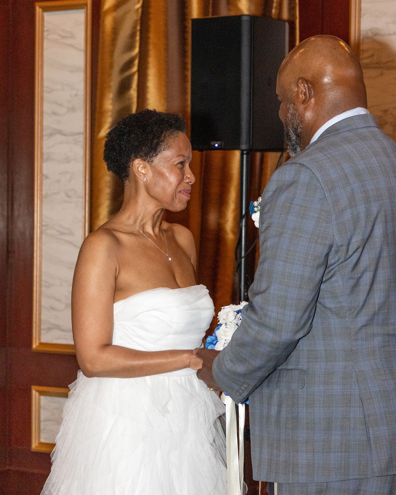Close-up of bride in white strapless dress exchanging vows with groom in gray plaid suit at wedding ceremony.