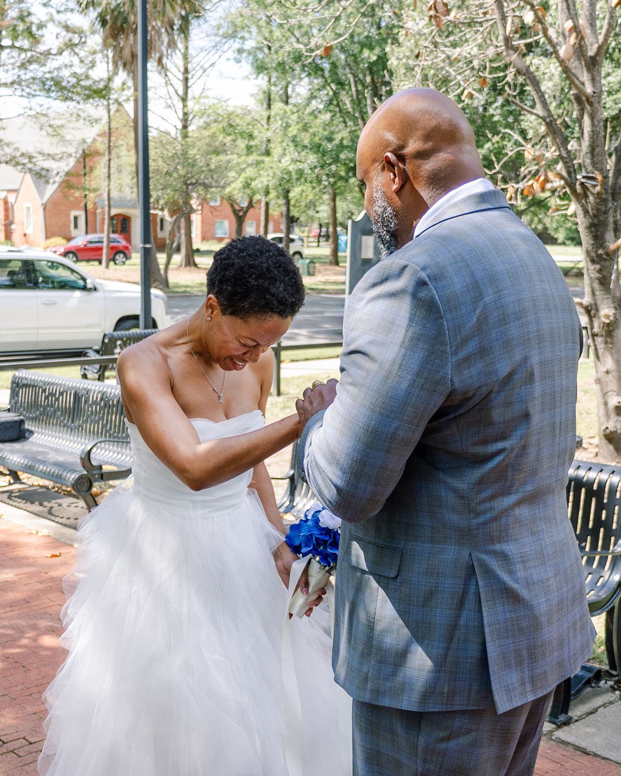 Emotional bride and groom share tender first look moment, bride bowing head while holding blue bouquet.