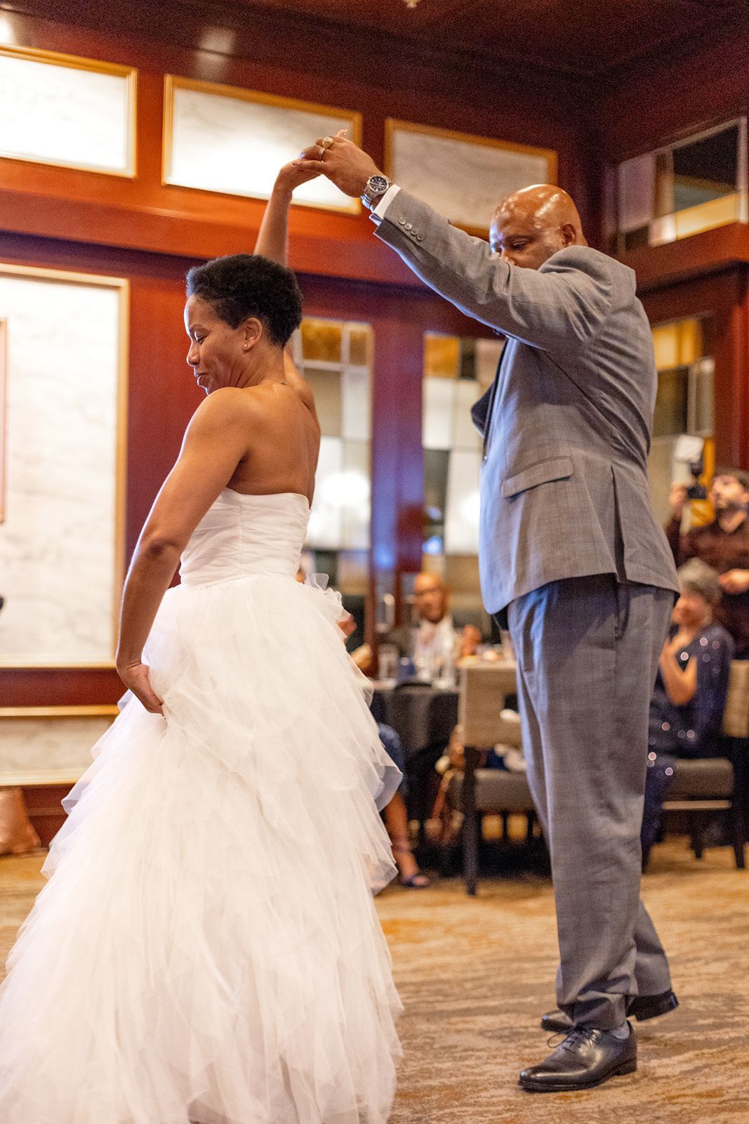 Groom in gray suit spinning bride in white wedding gown during first dance.