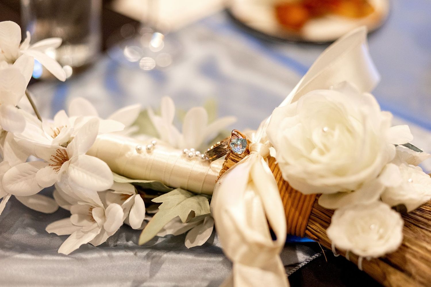 White floral decorations with roses and lilies arranged on a soft blue surface create an elegant wedding setting.