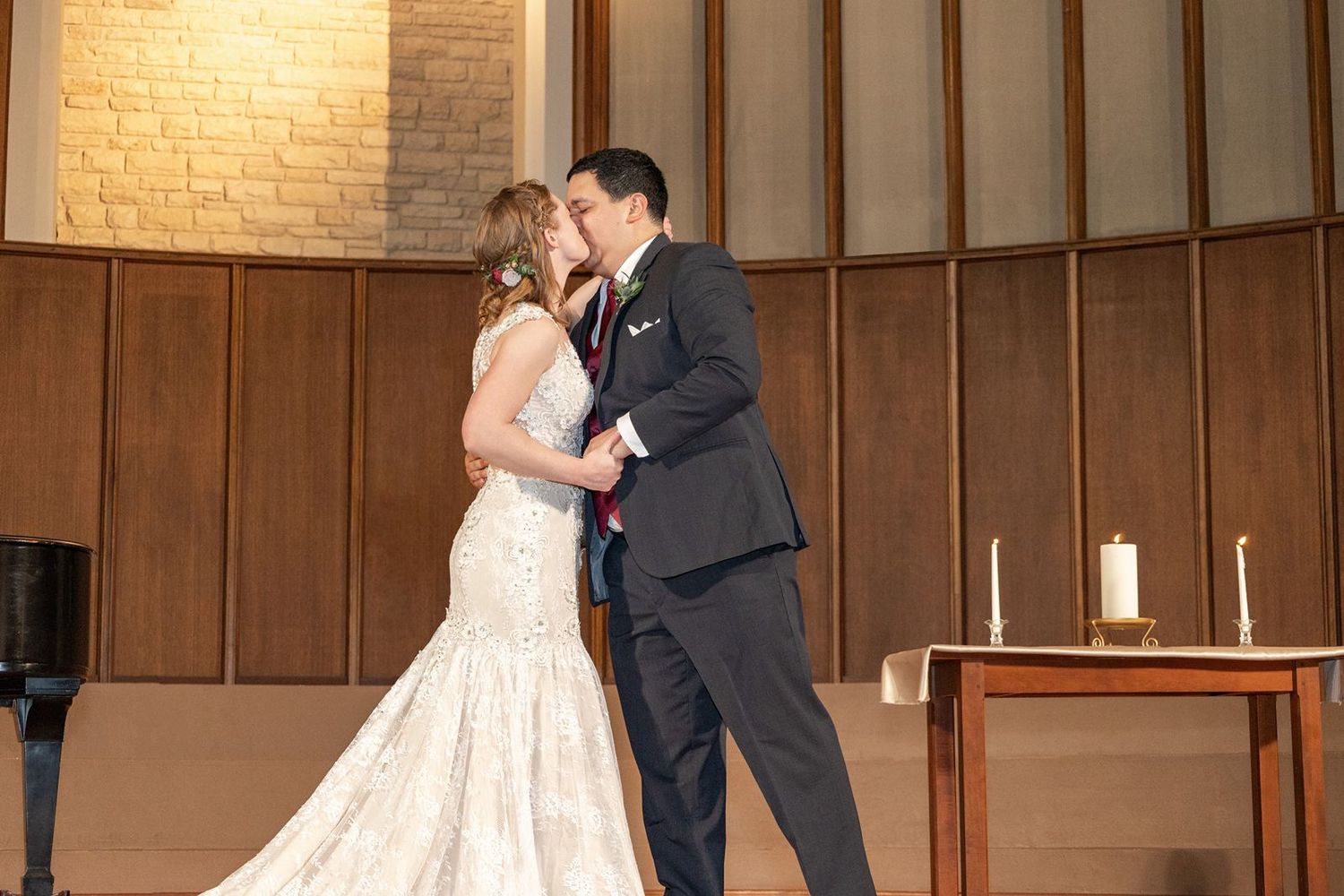 Bride and groom share first kiss at church altar during wedding ceremony.