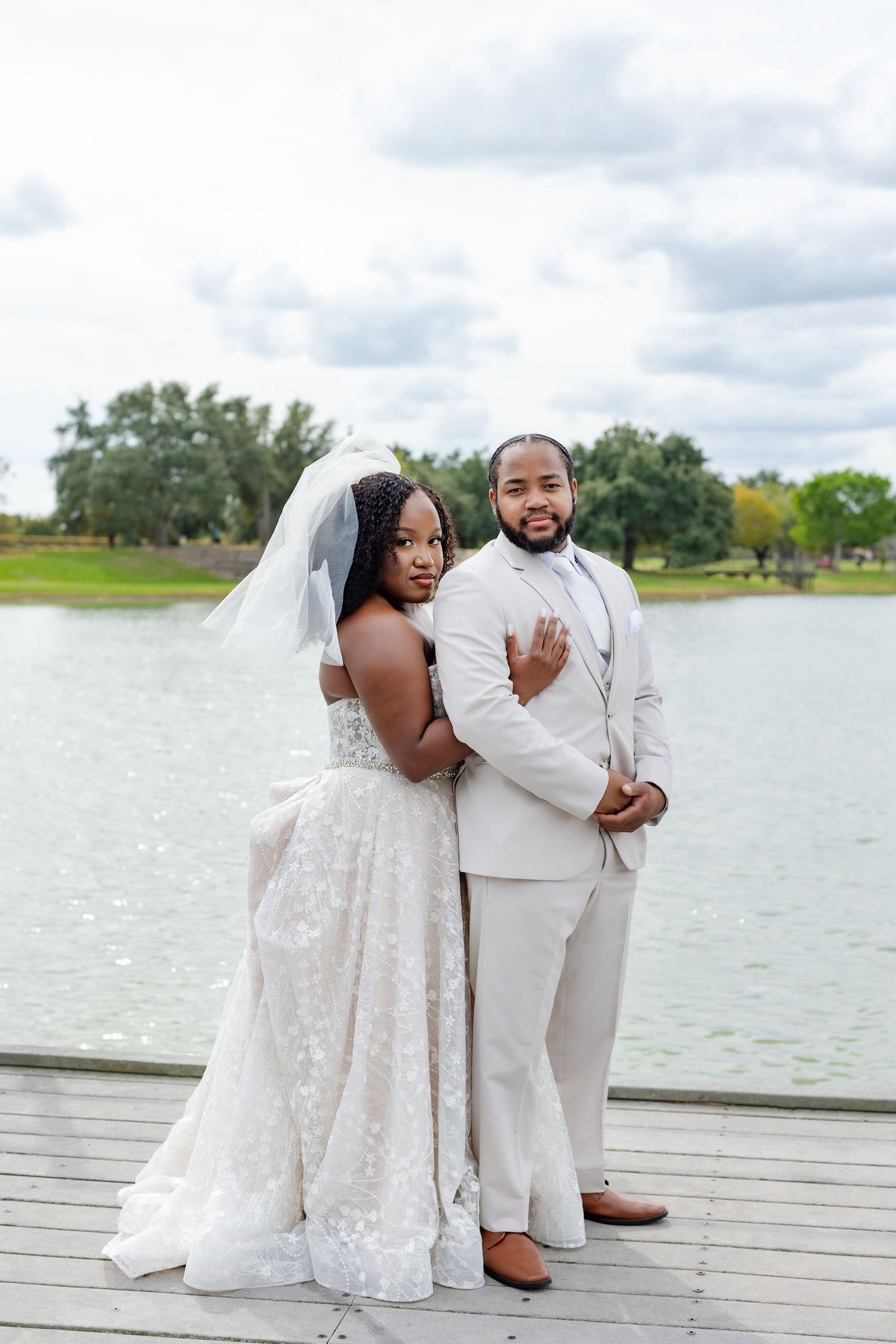 Wedding couple posing playfully on wooden dock with lake backdrop.