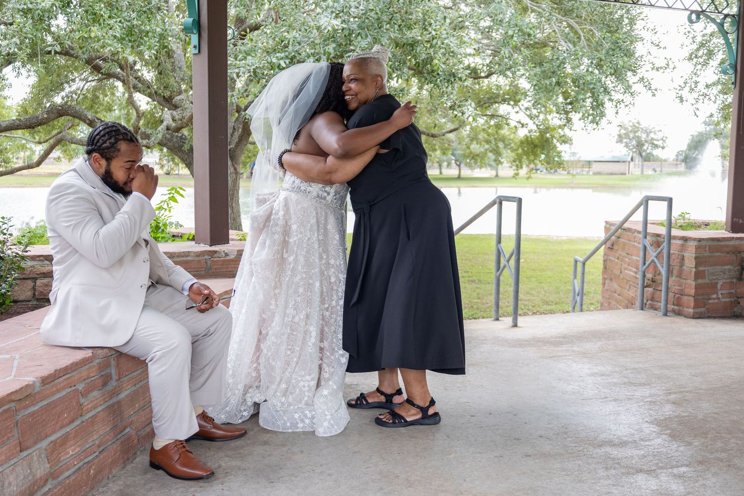 An emotional moment during a wedding ceremony as people embrace under a covered pavilion.