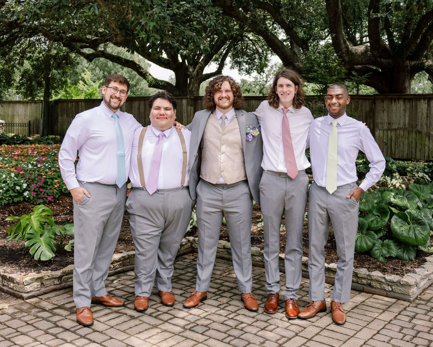Wedding party wearing matching gray suits and brown shoes lined up showing their shoes in a garden setting.