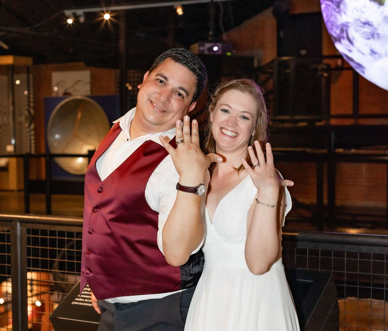 Newlyweds joyfully show off their wedding rings at a museum reception venue.