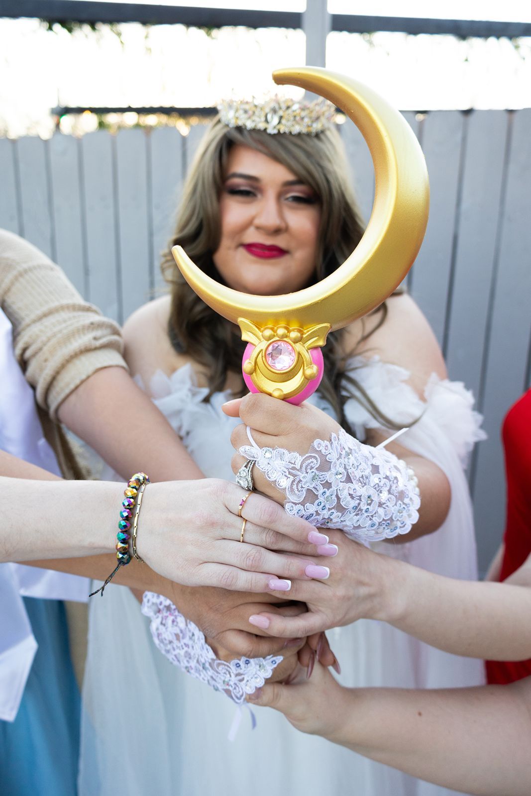 Woman cosplaying as Sailor Moon in white dress holds golden crescent wand with friends at cosplay event.