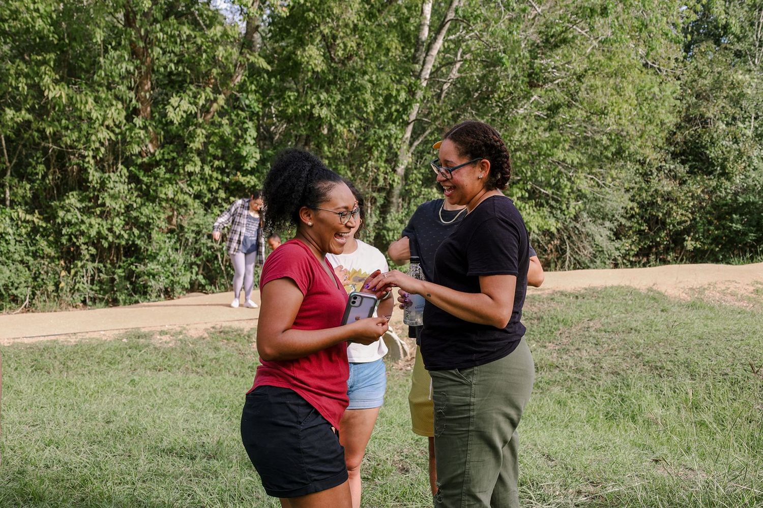 Two women laughing and sharing a joyful moment outdoors on a sunny day near a dirt path.