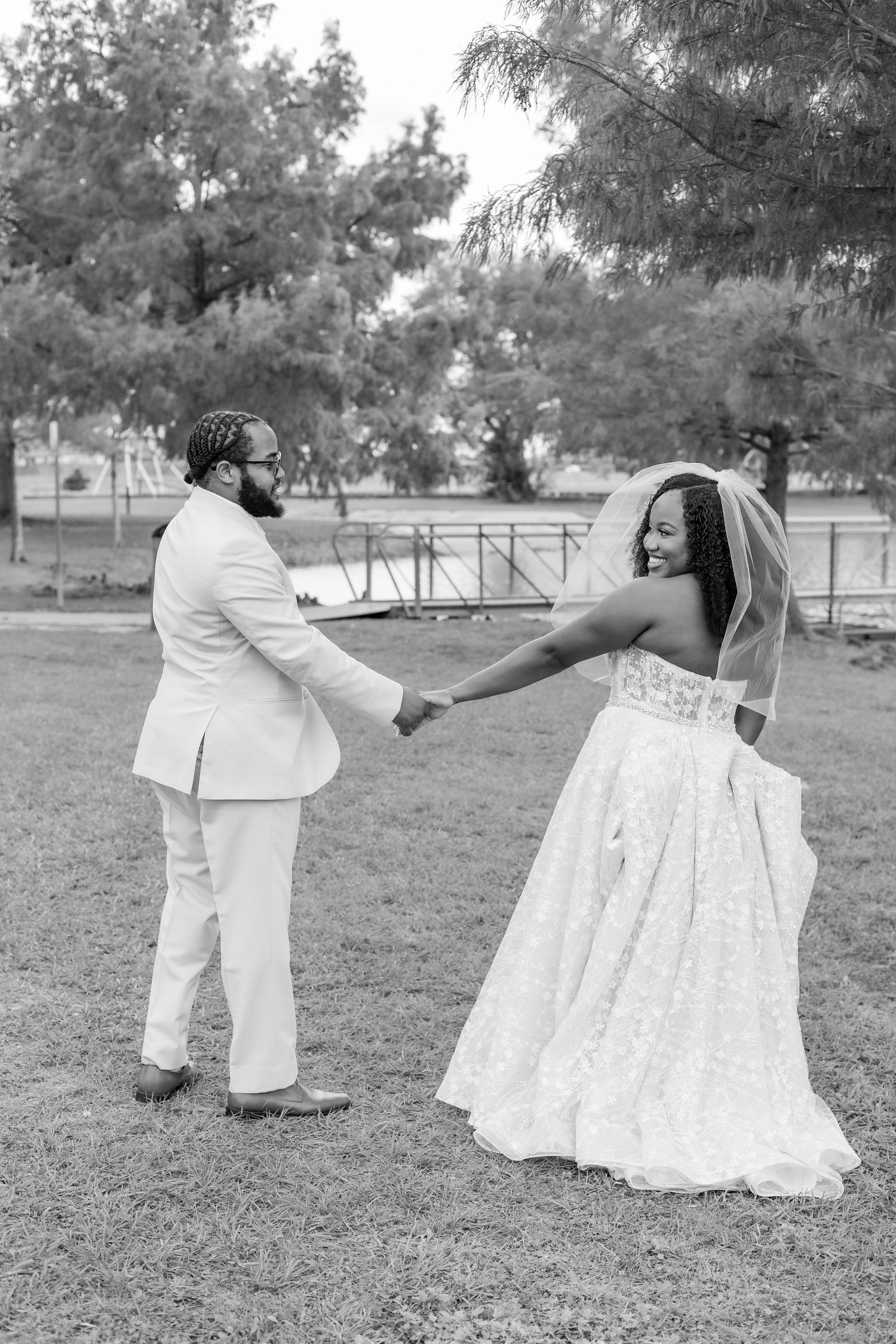 Black and white wedding photo of couple playfully posing in outdoor setting.