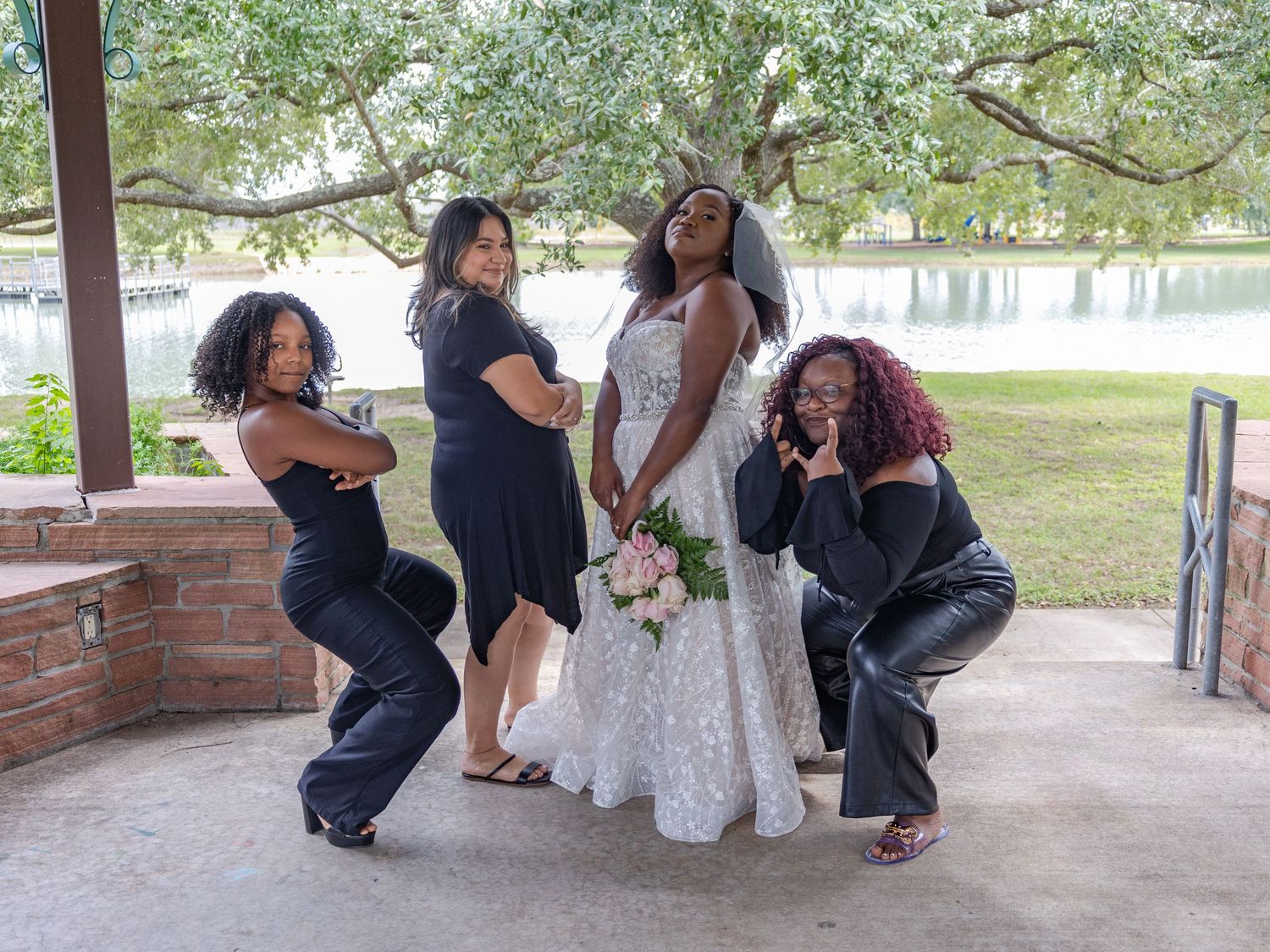 Bridal party in coordinating black dresses and white gown gather for casual photos.