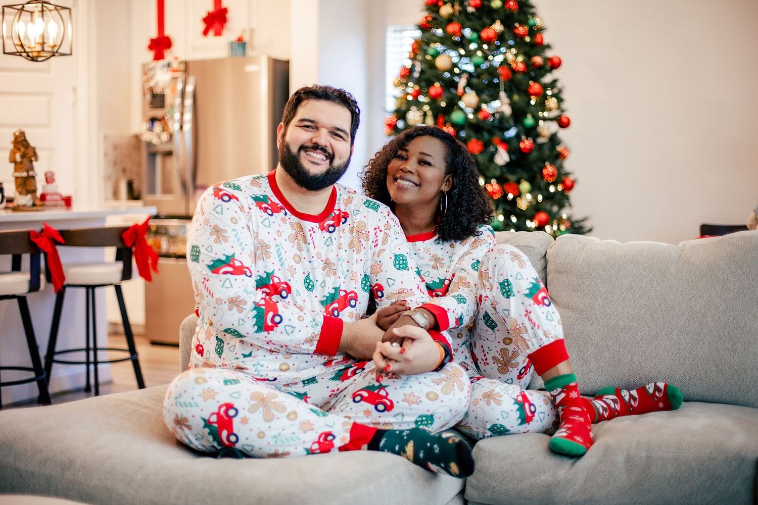 Family wearing festive red and white holiday pajamas lounging together on sofa near Christmas tree.