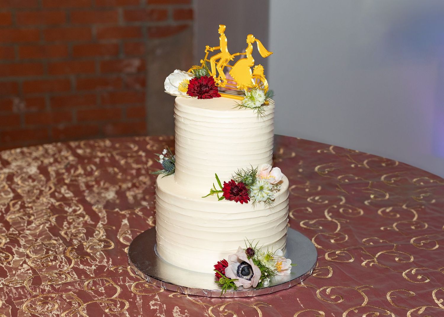 White wedding cake with textured frosting and burgundy floral decorations displayed on an elegant table.
