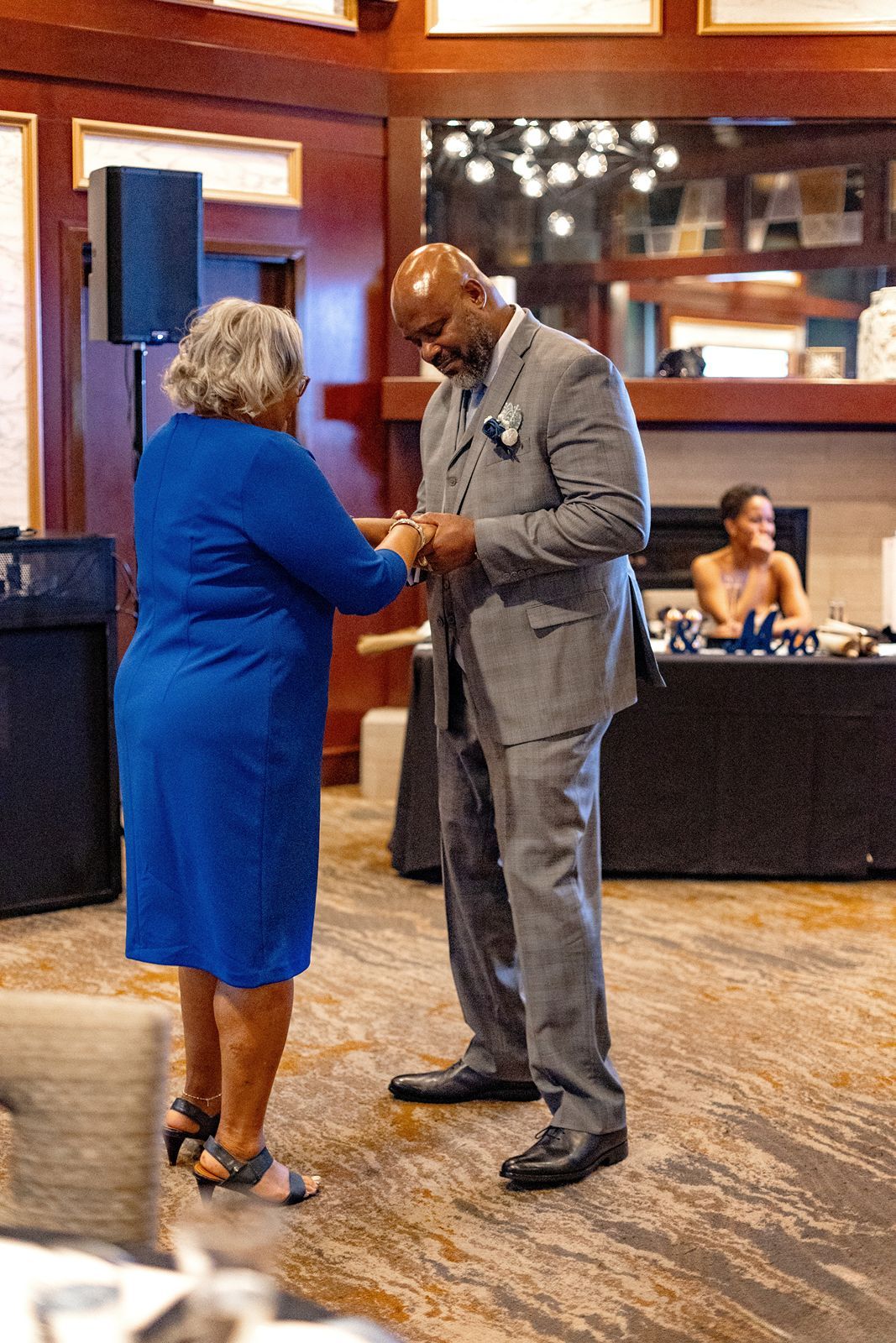 Groom in gray suit dancing with elderly woman in blue dress at wedding reception.