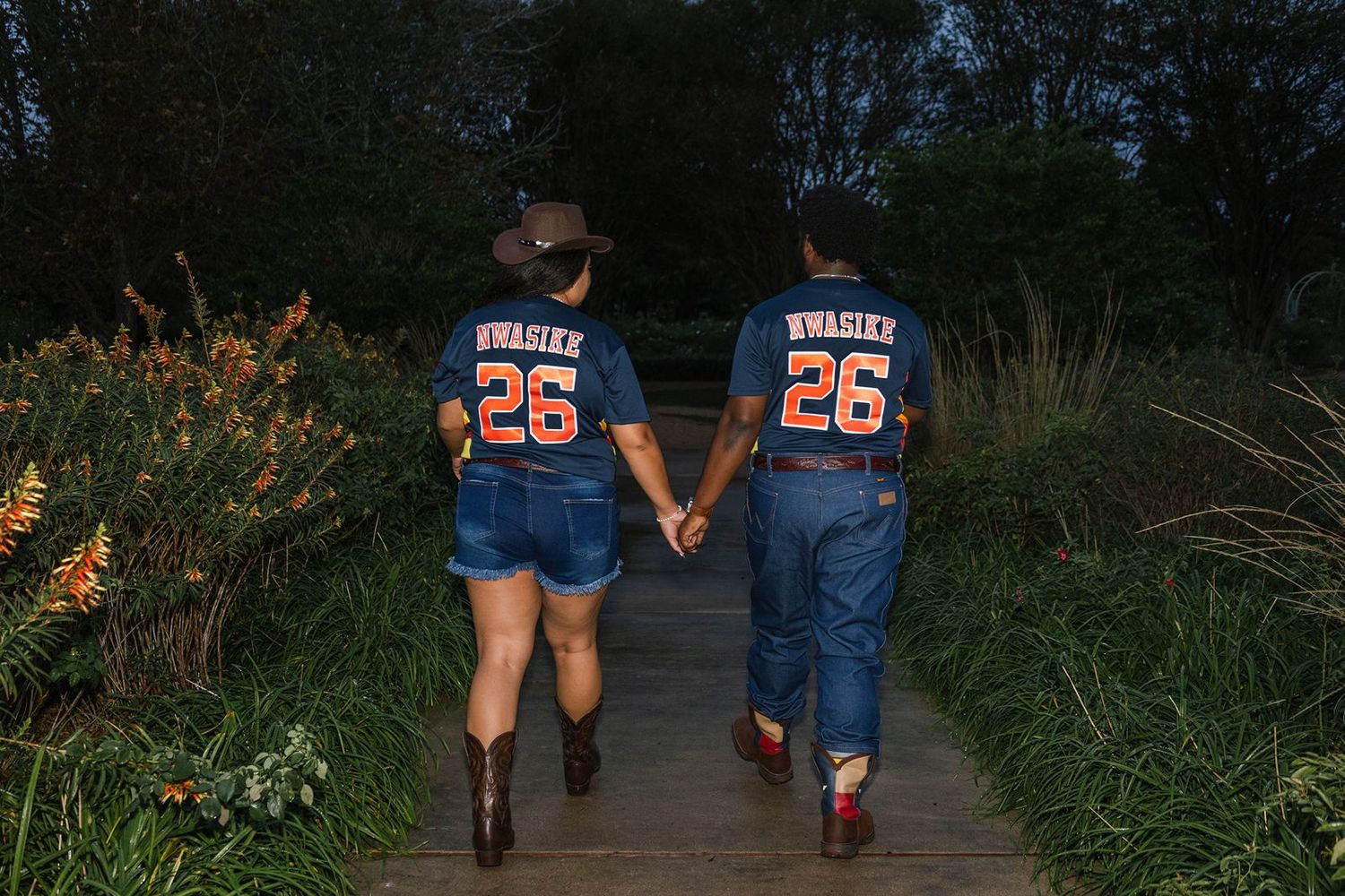 Two people wearing matching jerseys walk along an outdoor path surrounded by autumn foliage and pumpkins.