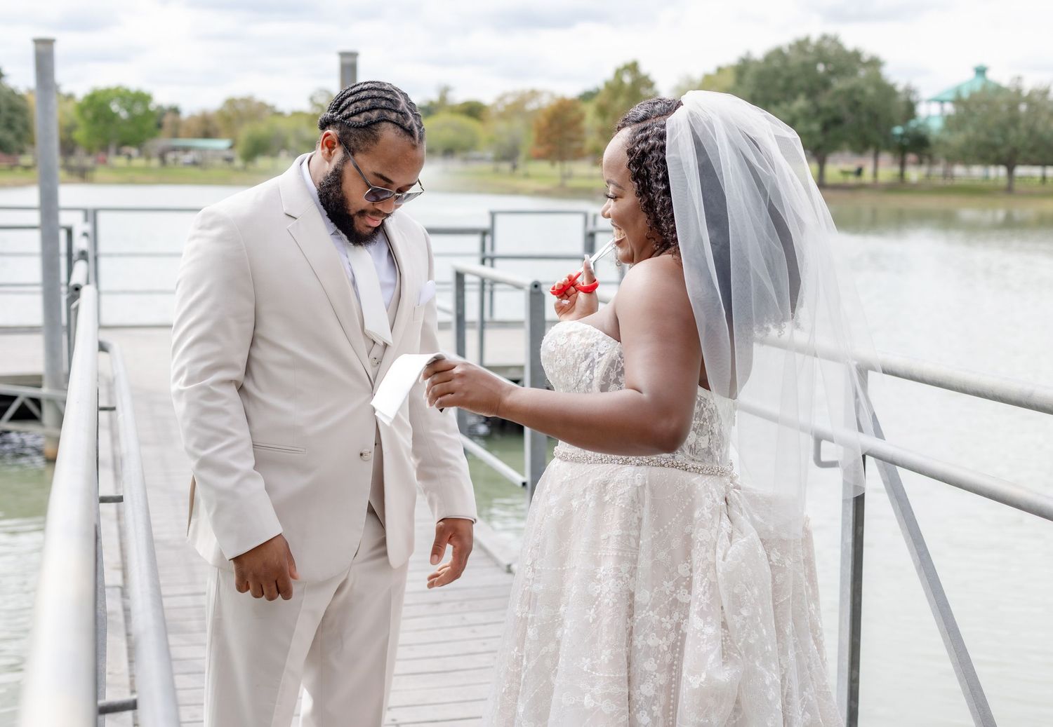 Newlyweds share candid moments on wooden pier overlooking water.