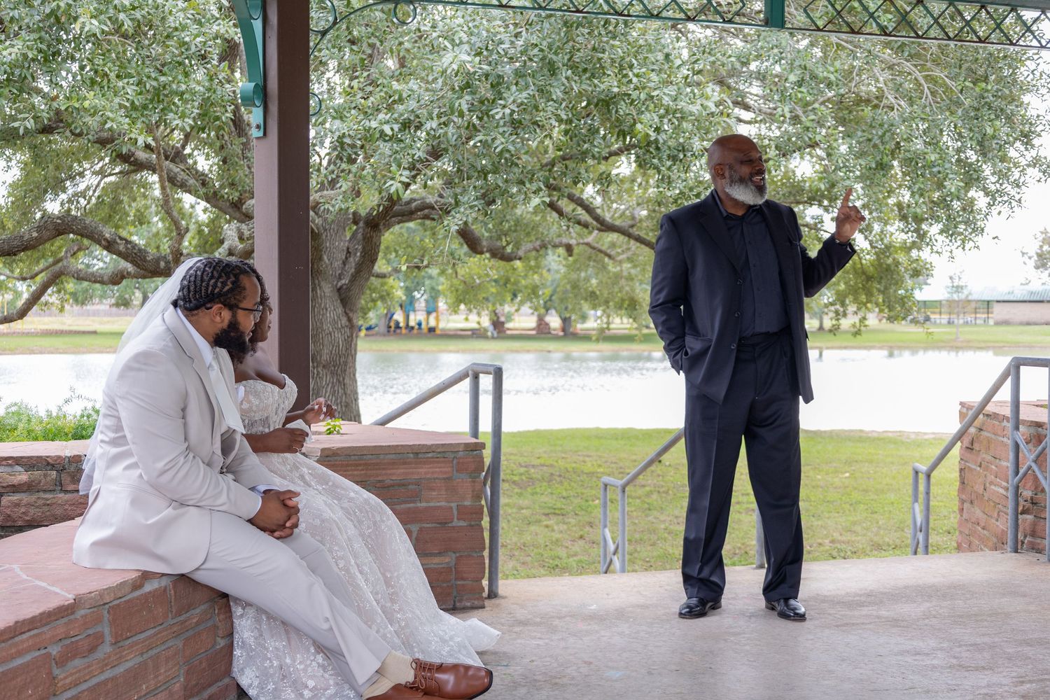 Wedding guests and party members gather under wooden pavilion for celebration photos.