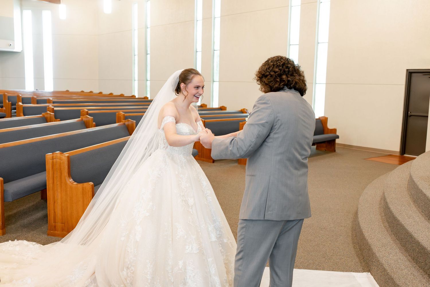 Bride and partner share an intimate first look moment in a church sanctuary with wooden beams and blue pews.