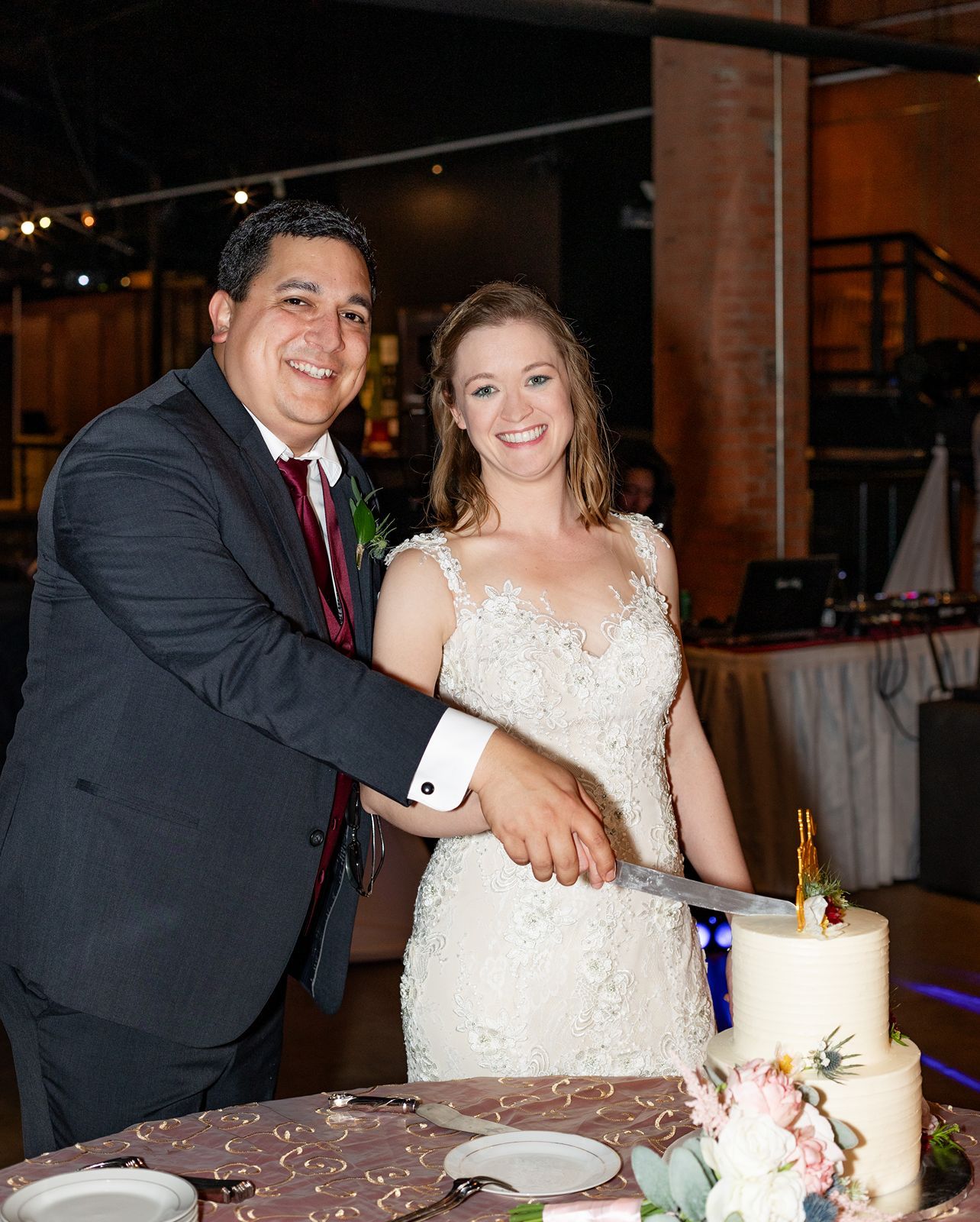 Smiling bride and groom cutting white wedding cake at reception.