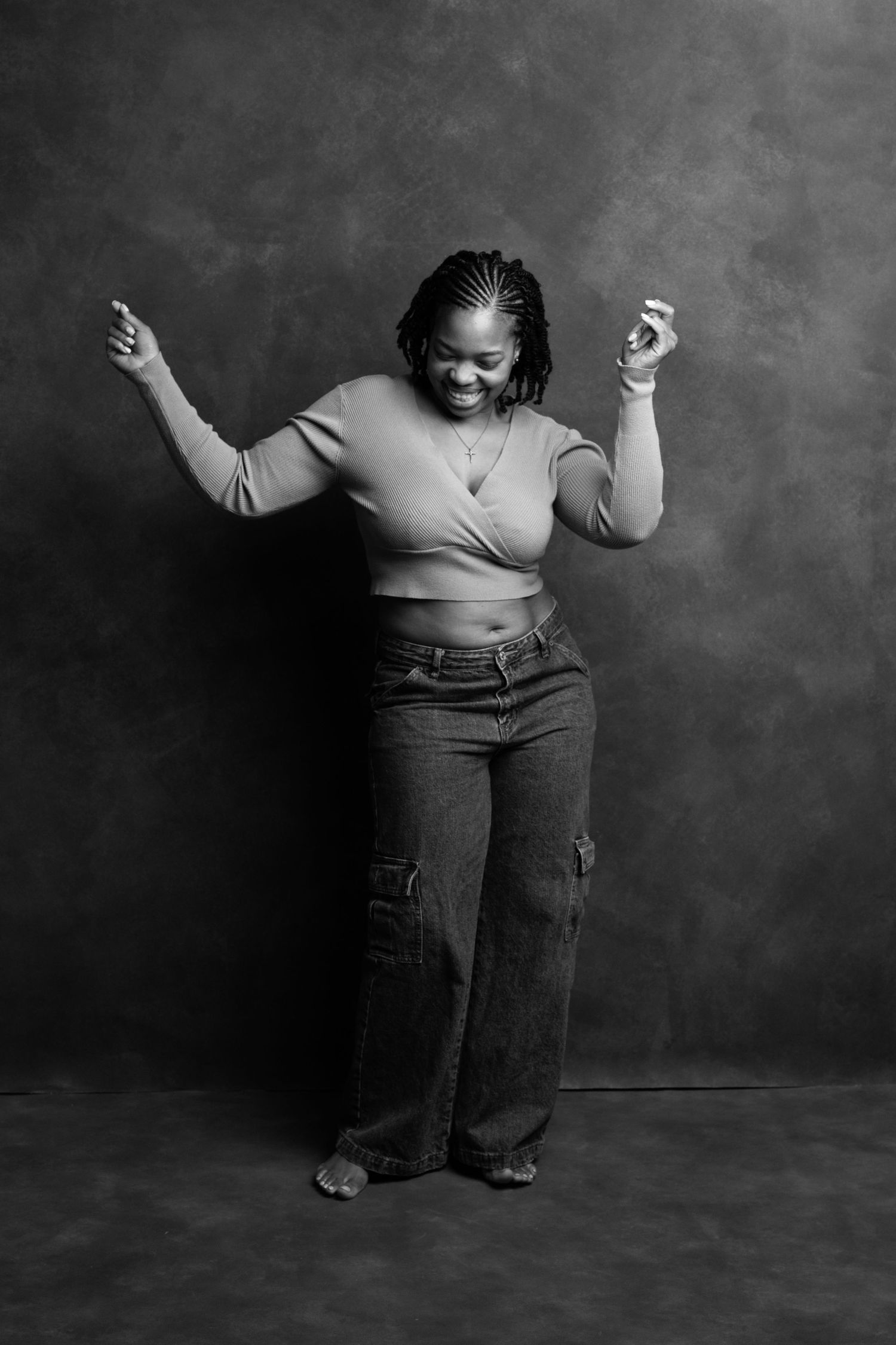 Black and white photo of a joyful woman dancing in jeans and crop top against a studio backdrop.