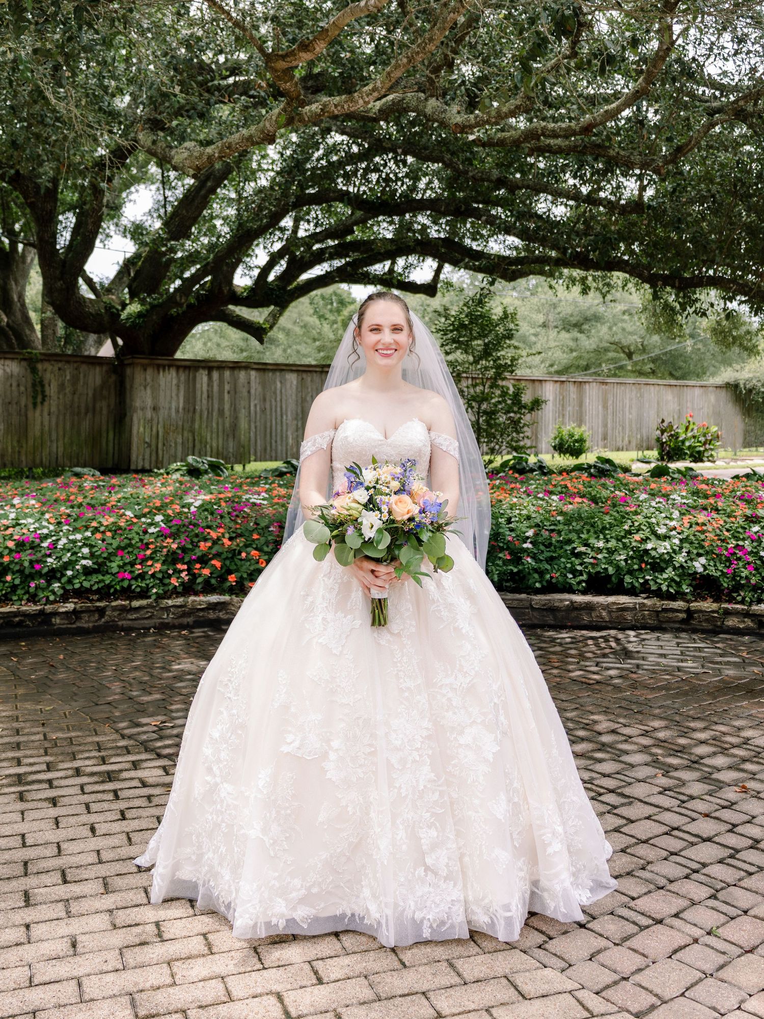 A wedding dress silhouette photographed in a garden setting with brick pathways and flowering bushes.