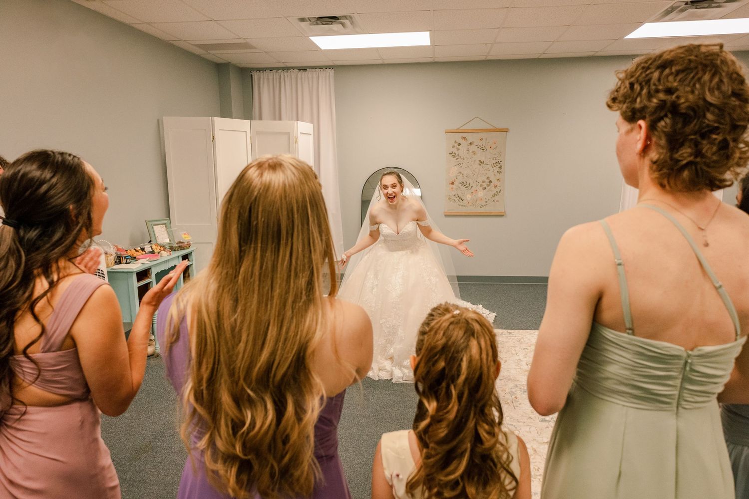 Group of women in coordinated bridesmaid dresses gathered in a bridal preparation room.