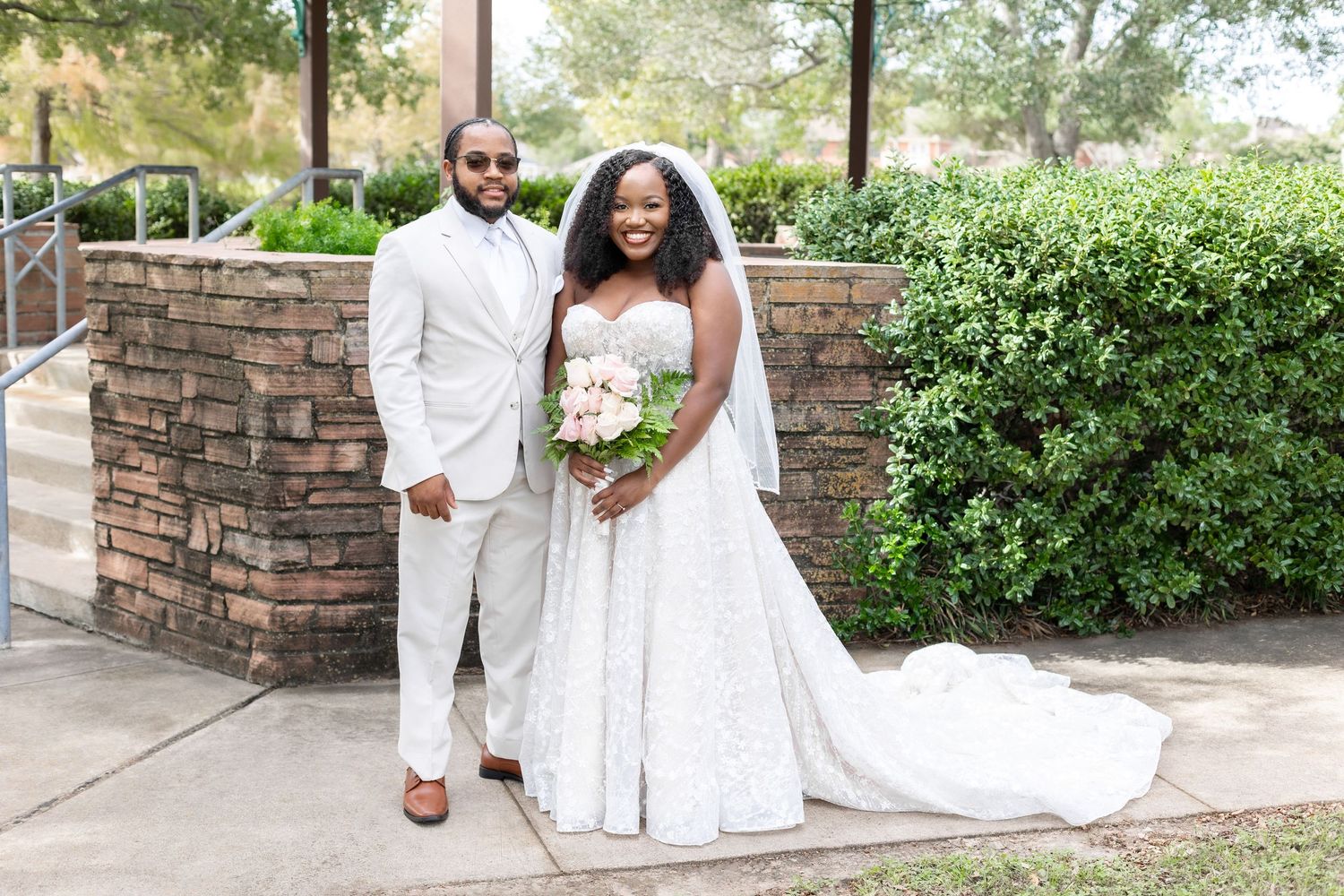 A joyful wedding couple shares intimate moments in an outdoor garden setting wearing white formal attire.