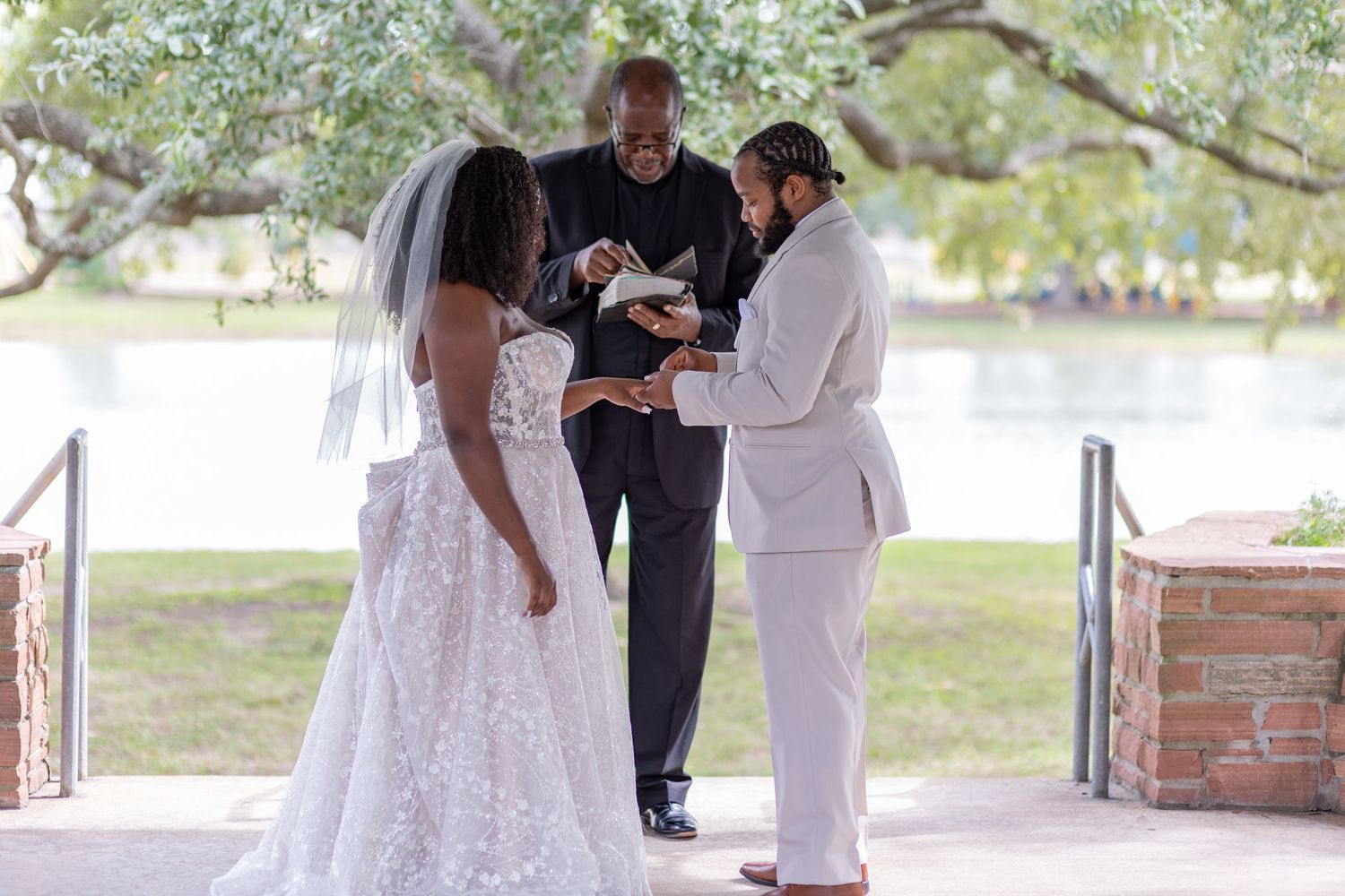 A wedding ceremony takes place outdoors with the couple and officiant standing under a covered area.
