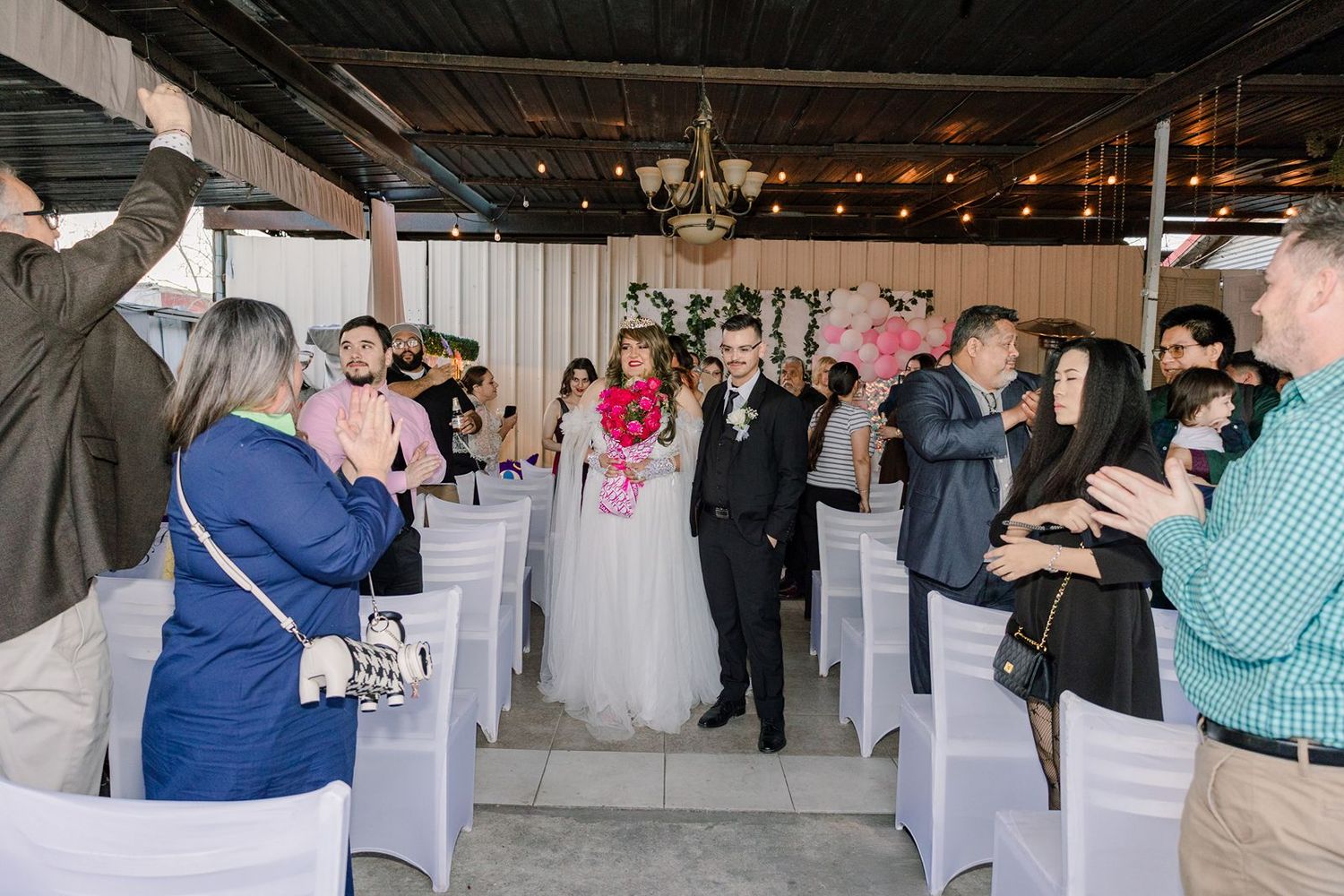 Newlyweds walk down aisle as guests applaud at elegant indoor wedding reception venue.
