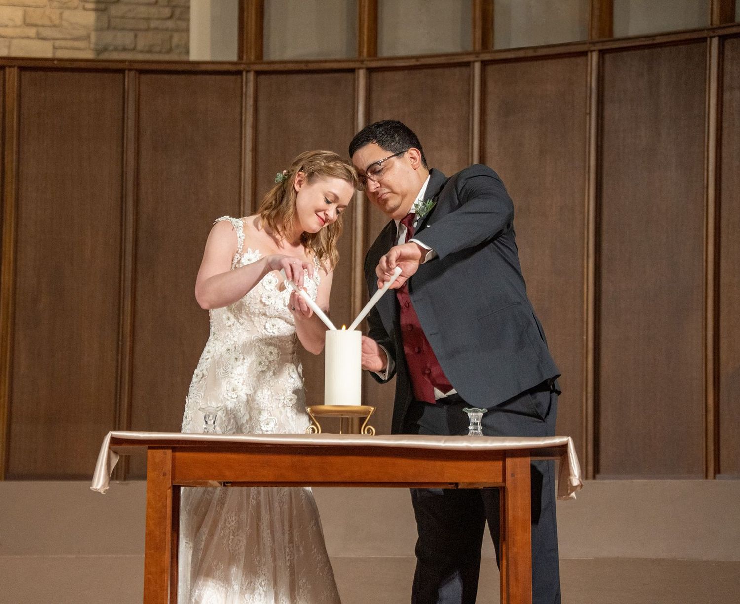 A wedding couple performs a unity ceremony ritual at their reception with wooden panels in the background.