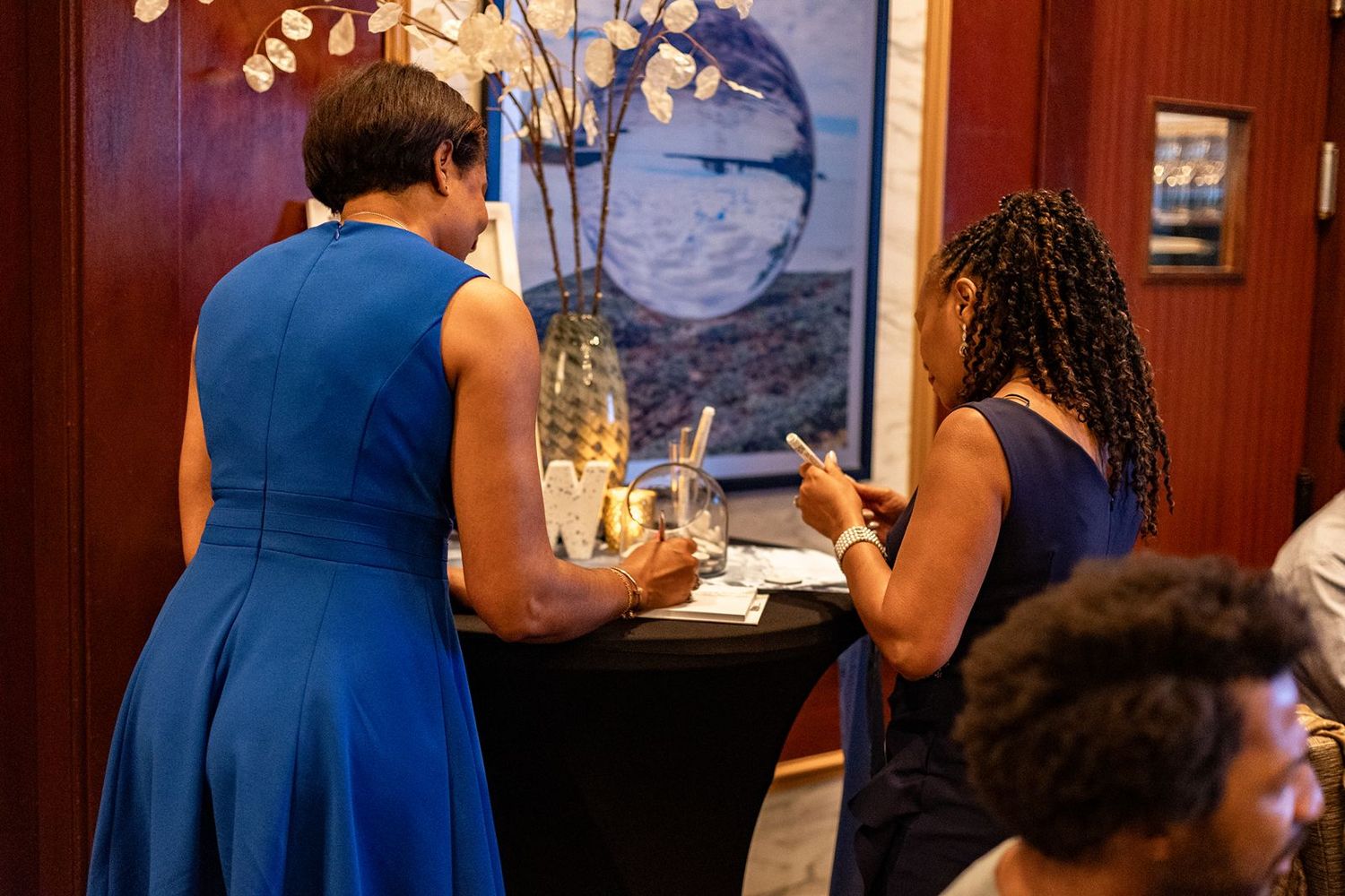 Two women in blue dresses stand at a cocktail table during an elegant wedding reception event.