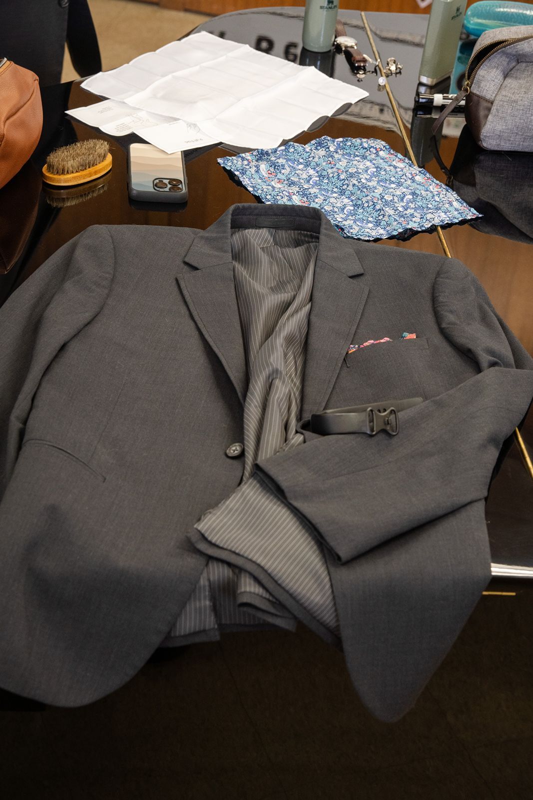 Gray suit jacket with blue floral pocket square laid out on a table for a wedding.