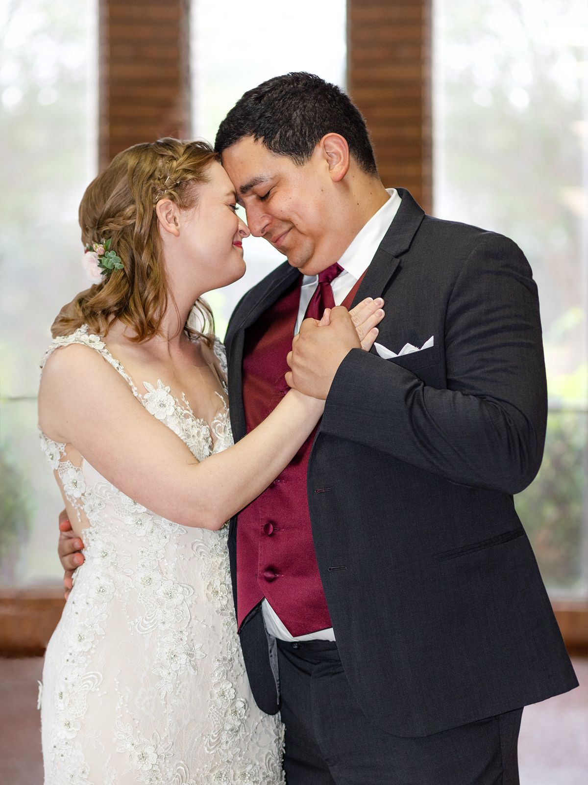 Bride and groom share an intimate first dance moment, touching foreheads in a sunlit venue.
